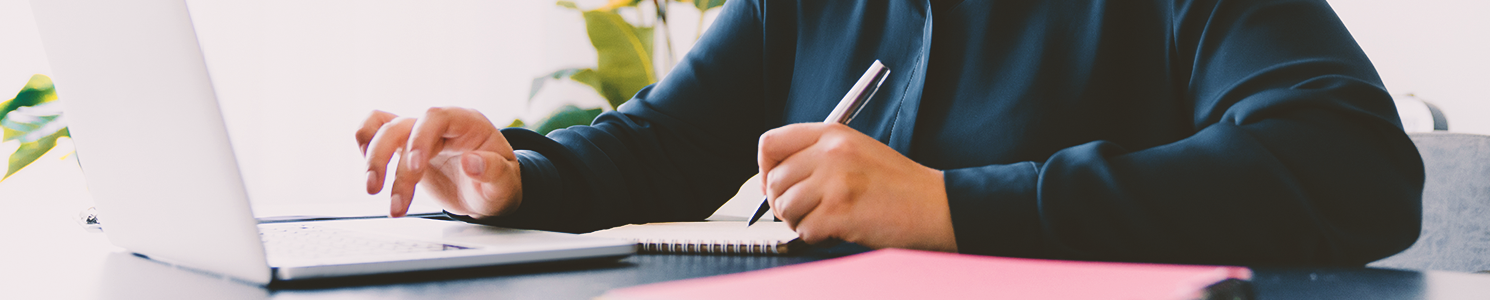 A business person writing down notes in front of a laptop