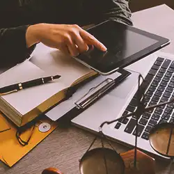 A lawyer using a tablet in front of a laptop with paperwork on the table