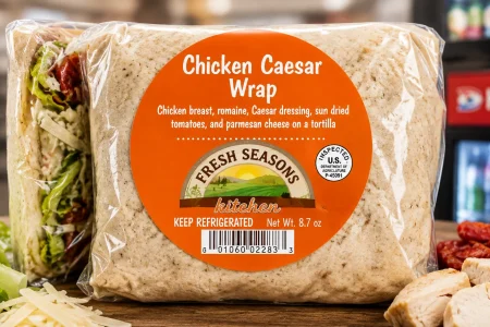 FRESH SEASONS Kitchen Chicken Caesar Wrap in clear packaging with its orange product label displayed in a convenience-store setting.