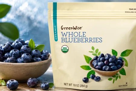 GreenWise Organic Whole Blueberries package displayed beside a bowl of fresh blueberries on a wooden surface.