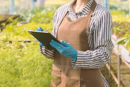 A scientist writing down on a clipboard outside in a farm while writing down how glyphosate harms DNA