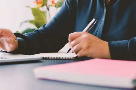 A lawyer writing down notes in front of a laptop