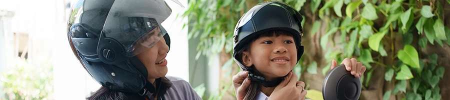 A mother putting a motorcycle helmet on her daughter