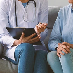 A doctor talking to a patient sitting down while holding a clipboard