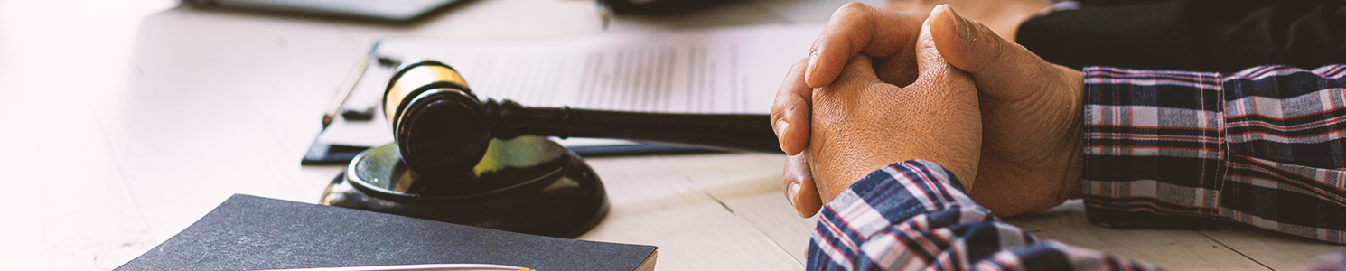 A person clasping their hands with a lawyer's gavel on the side