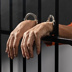A man who is behind bars and wearing handcuffs