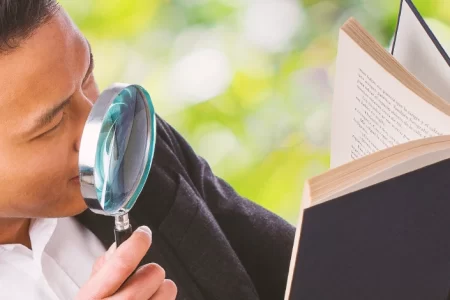 A person holding a magnifying glass to a book