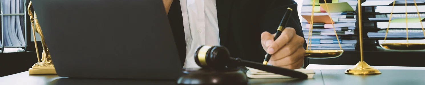 A lawyer using a laptop while taking down notes on the burden of proof during a roundup claim