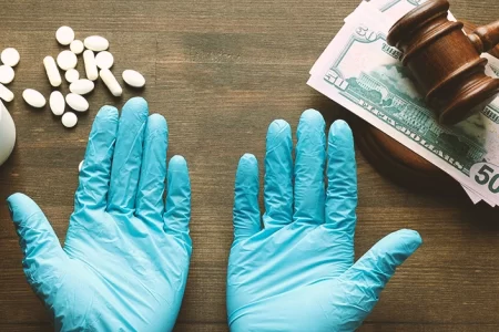 A surgeon with his hands out on a table with spilled pills and money under a gavel