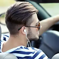 A person wearing stripe shirt using earphones while driving.