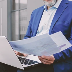 A lawyer looking at a laptop while holding paperwork